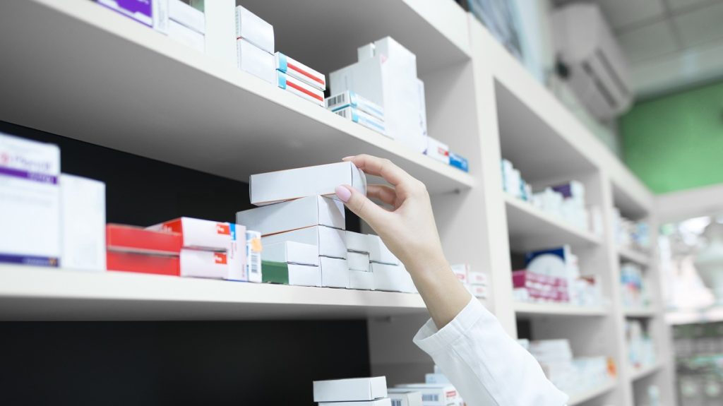 closeup view pharmacist hand taking medicine box from shelf drug store