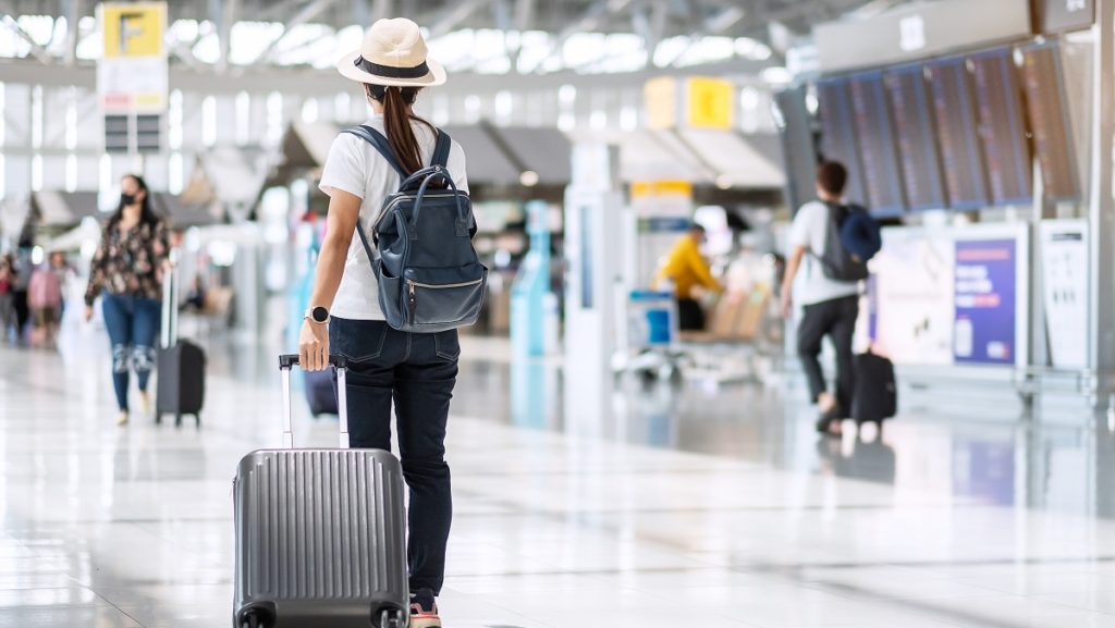 young female wearing face mask with luggage checking flight time airport