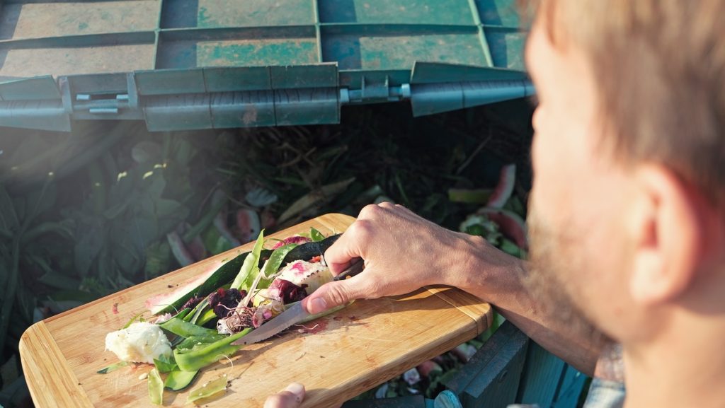 person throws kitchen food waste into compost heap ACJU8YE