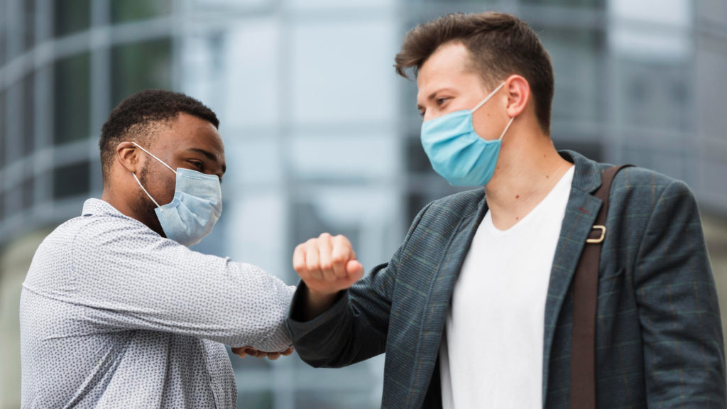 two colleagues touching elbows outdoors during pandemic copy