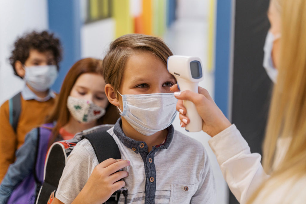 female teacher with medical mask checking student s temperature school copy