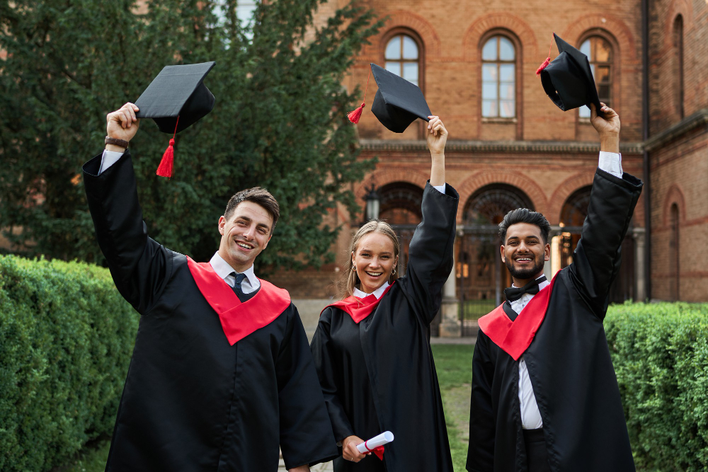 multinational graduates male female celebrating graduation university campus removing their graduation hats smiling camera