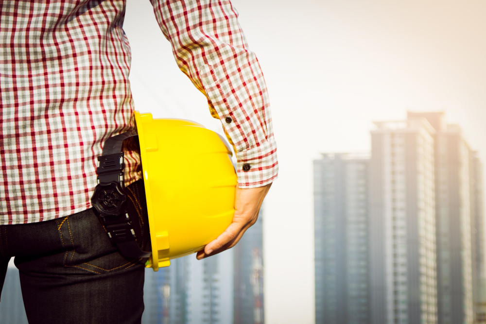 hand s engineer worker holding yellow safety helmet with building site background