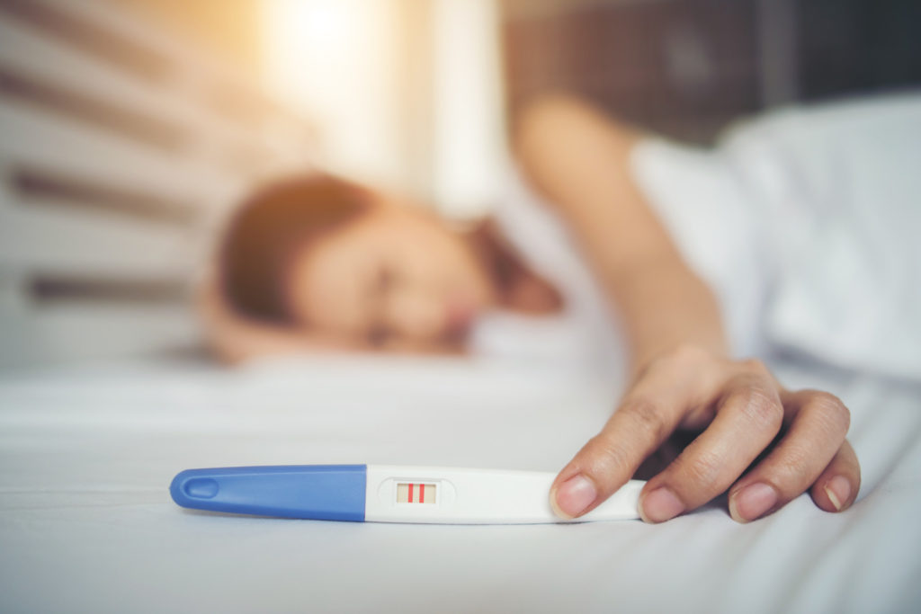 sad woman complaining holding pregnancy test sitting bed