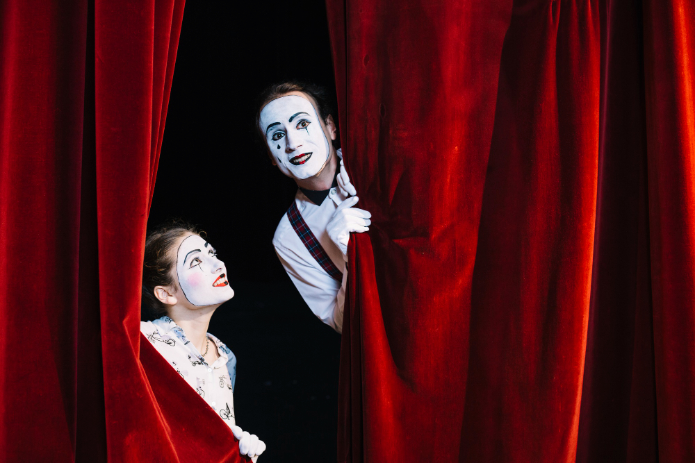 smiling female mime artist looking male mime artist peeking from curtain