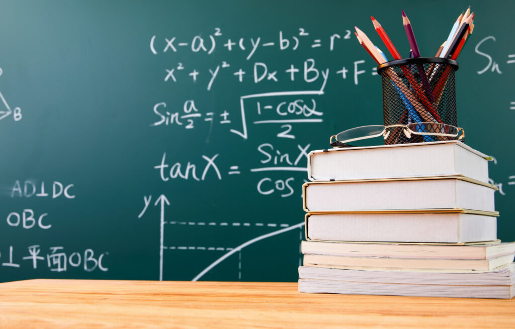 stack books with pencil holder glasses against chalkboard